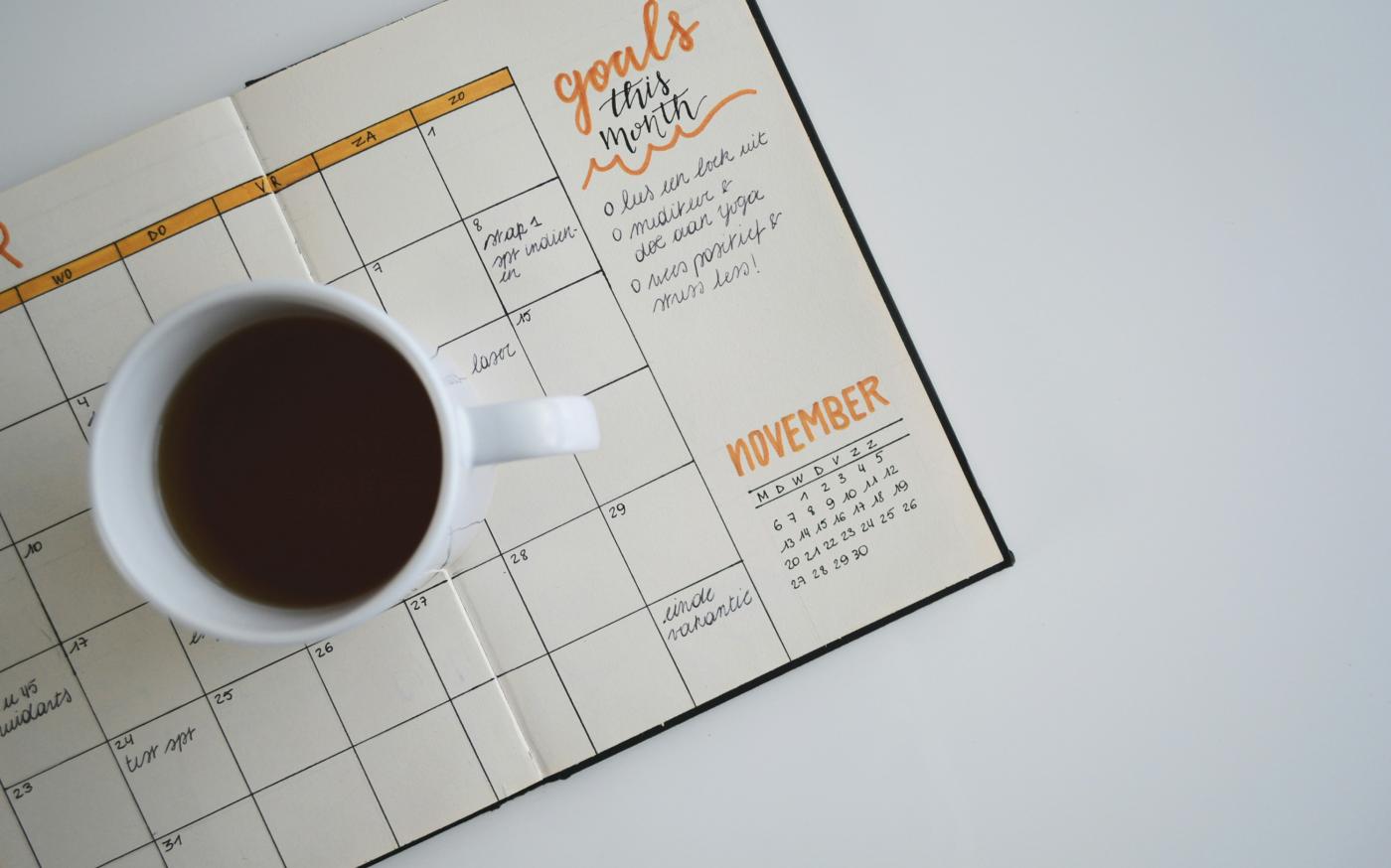 white ceramic mug with coffee on top of a planner by Estée Janssens courtesy of Unsplash.